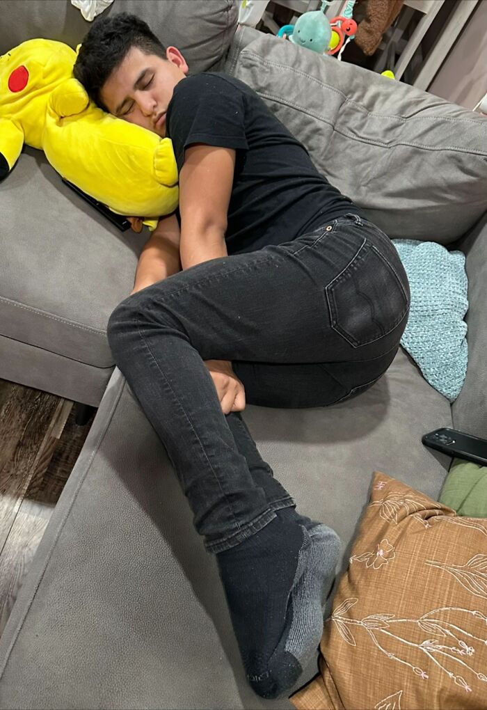 Young man lying curled up awkwardly on a couch with a yellow plush pillow, showing hilariously awkward body language.