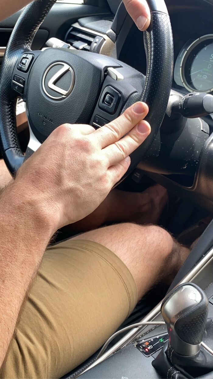 Man’s awkward body language showing fingers placed unusually on a steering wheel inside a Lexus car.
