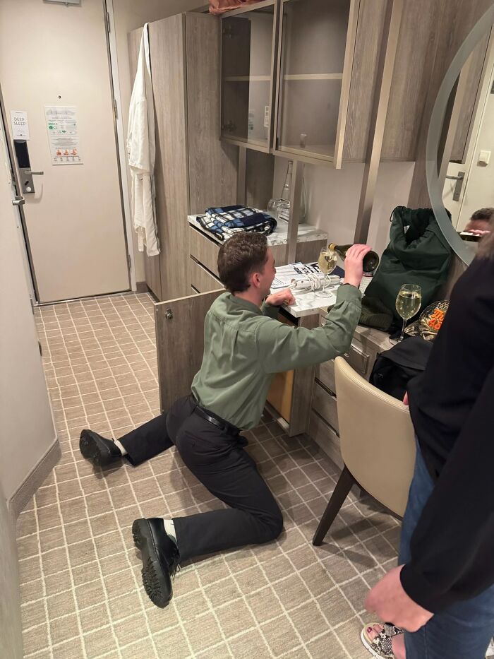 Man displaying hilariously awkward body language while pouring a drink in a small room with scattered items around.