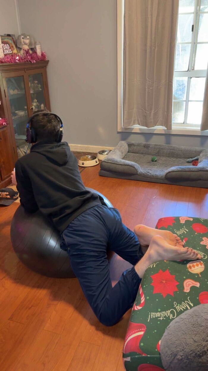 Man displaying hilariously awkward body language while lying on an exercise ball wearing headphones indoors on hardwood floor.