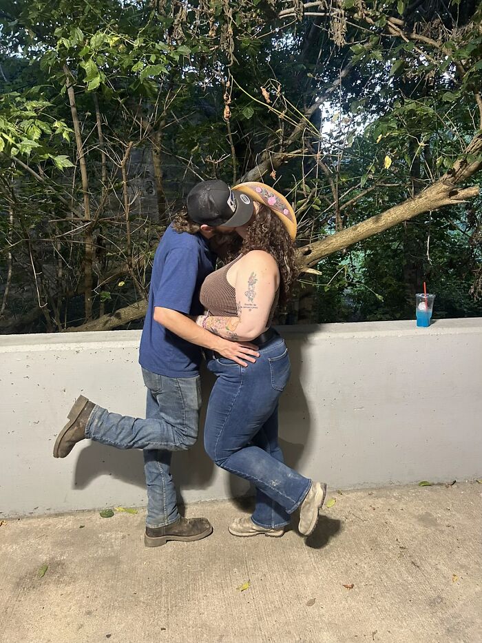 Couple sharing a kiss outdoors with awkward body language causing a humorous and relatable moment between them.