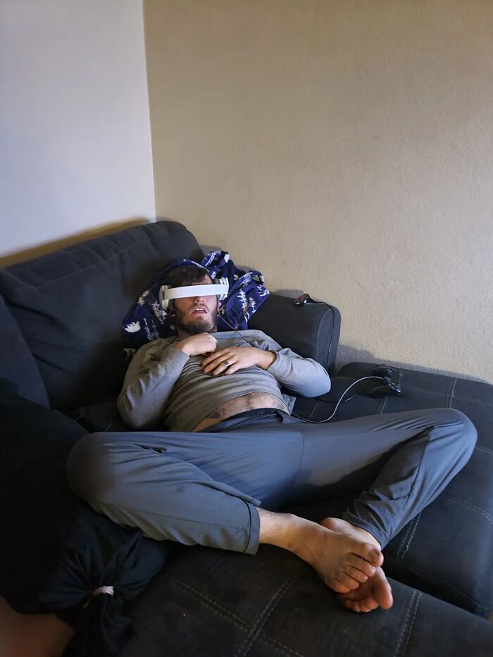 Man displaying hilariously awkward body language while lounging on a couch with video game controller nearby.