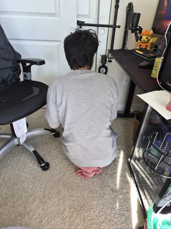 Man sitting awkwardly on his feet with poor body language in a casual room setting, showing awkward posture.