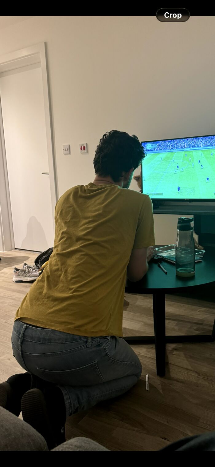 Man kneeling awkwardly in front of TV watching soccer, showing hilariously awkward body language giving the ick.
