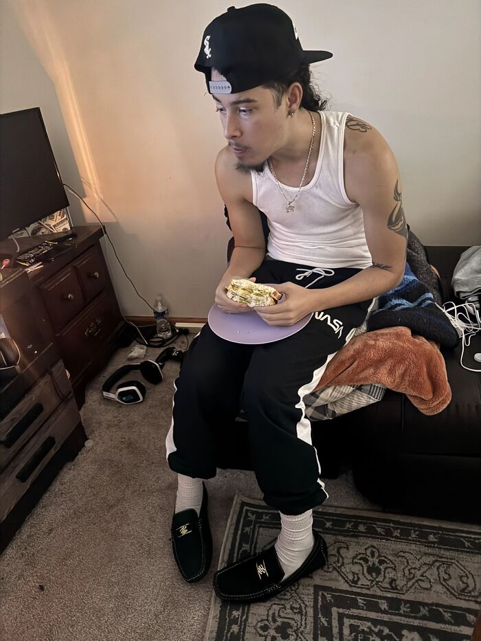 Young man sitting awkwardly on couch eating sandwich, showing awkward body language typical in men giving women the ick.