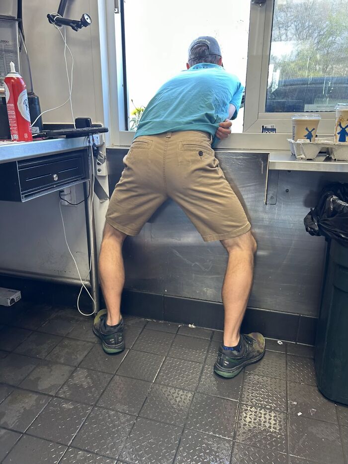 Man in shorts and sneakers leaning awkwardly over a counter, displaying hilariously awkward body language.