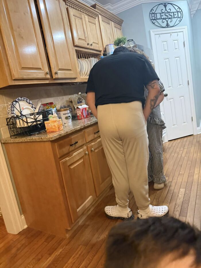 Man displaying awkward body language leaning over in a kitchen while interacting with a woman in casual clothing.