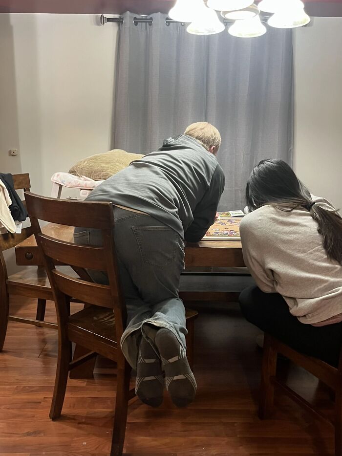 Man leaning awkwardly over a table while a woman sits nearby, showcasing men's hilariously awkward body language.