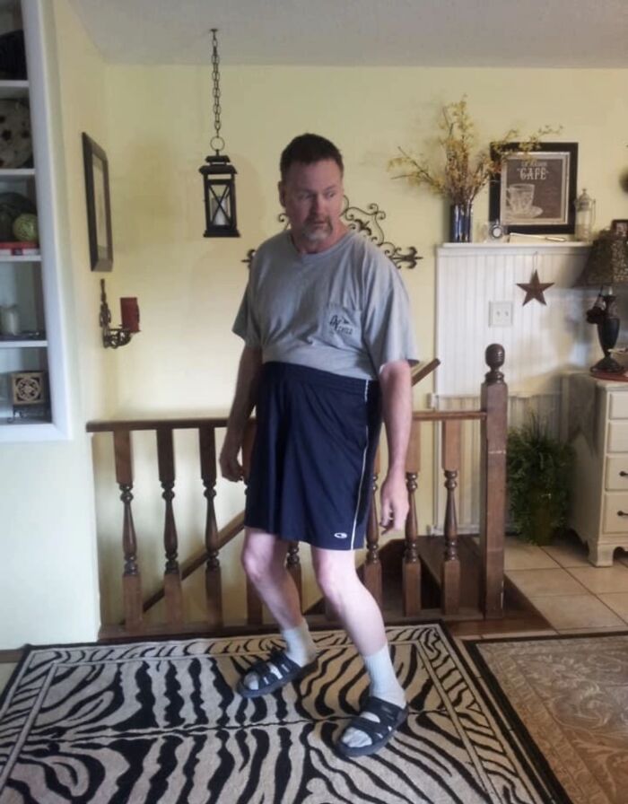 Man wearing mismatched clothes and sandals with socks inside a home, displaying awkward body language that gave women the ick.