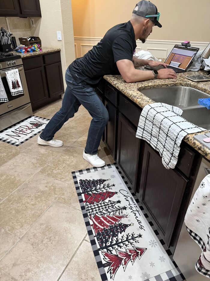 Man leaning awkwardly over kitchen counter using laptop, displaying hilariously awkward body language that gave women the ick.
