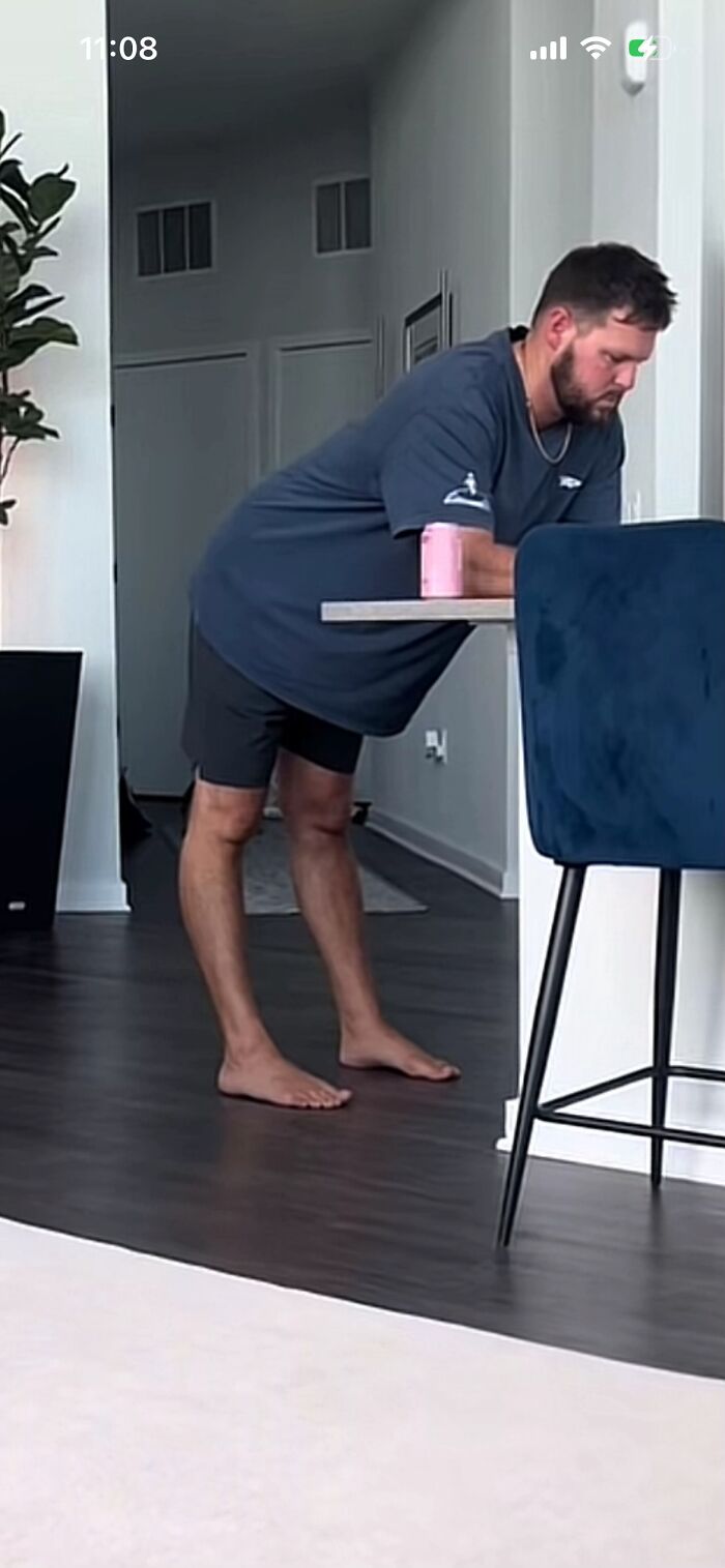 Man showing awkward body language, leaning forward barefoot in casual home setting with drink on table nearby.