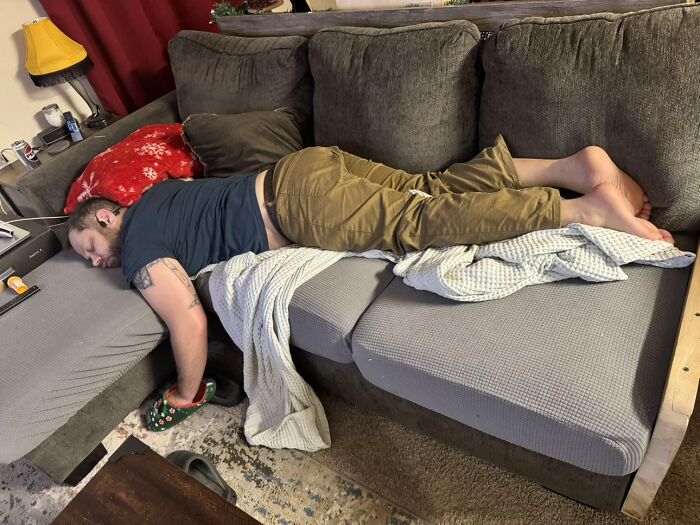 Man displaying hilariously awkward body language lying sprawled on a couch, giving an uncomfortable vibe often disliked by women.