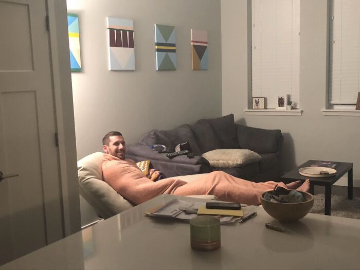 Man wrapped awkwardly in a blanket on a chair displaying hilarious body language in a casual living room setting