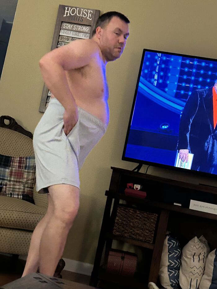 Man in gray shorts showing awkward body language indoors near TV and couch, highlighting awkward men’s body language moments.