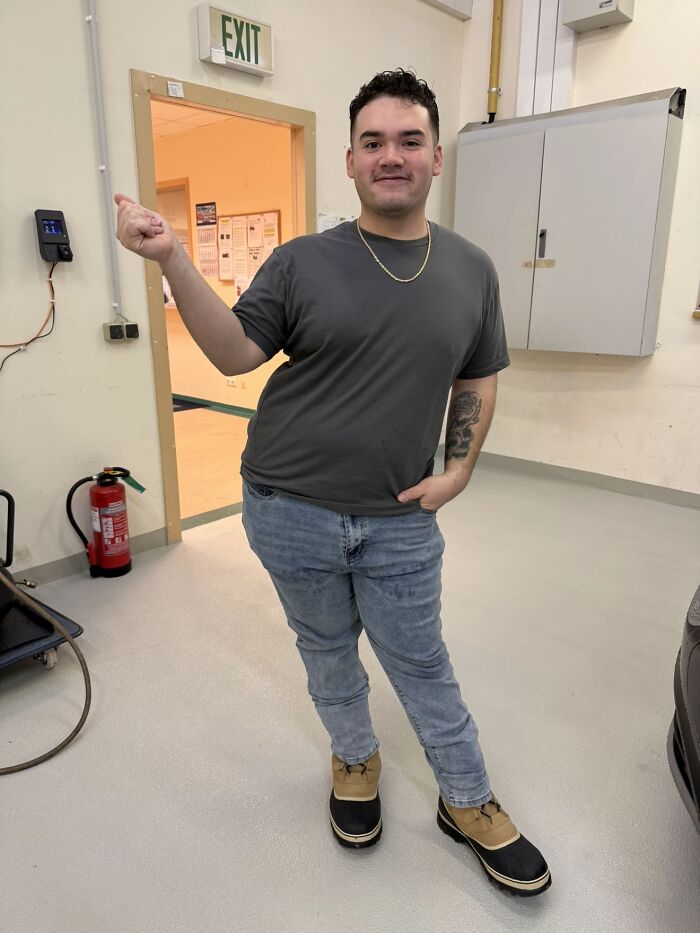 Man displaying awkward body language indoors, wearing jeans, a gray shirt, and tan black boots, giving women the ick.