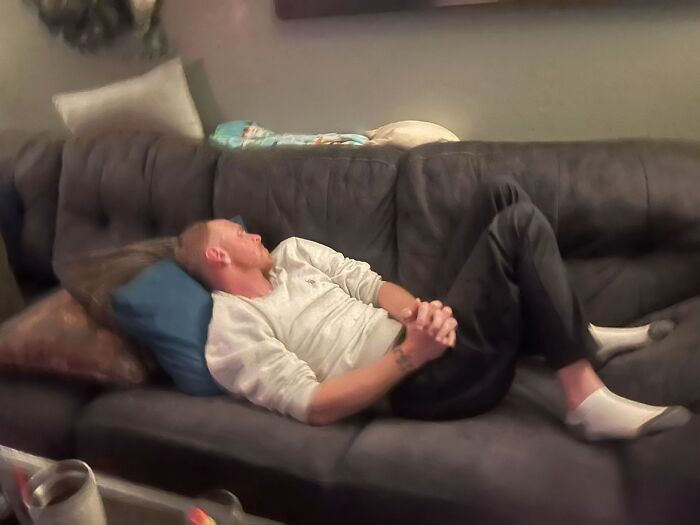 Man awkwardly lying on a couch with folded hands and bent knees showing awkward body language at home.