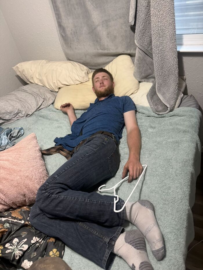 A man lying awkwardly on a bed holding a clothes hanger, displaying hilariously awkward body language.