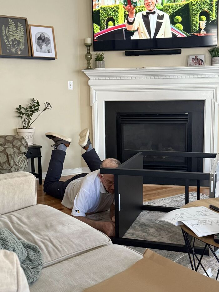Man displaying hilariously awkward body language while assembling furniture on the floor in a living room setting.