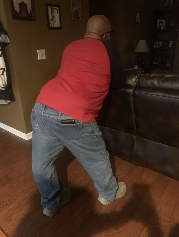 Man in red shirt and jeans striking an awkward pose by a couch, showcasing hilariously awkward body language.