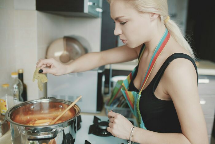 Young woman cooking in kitchen, adding herbs to pot, illustrating funny and harmless conspiracy theories concept.