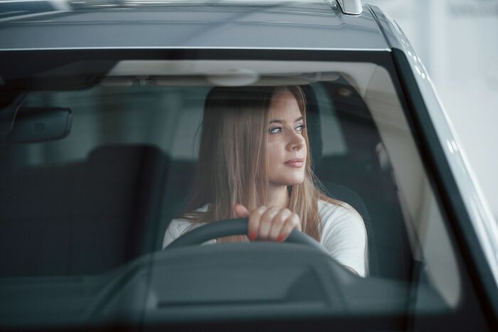 Young woman behind the steering wheel of a car, looking outside with a thoughtful expression, witnessing something strange.