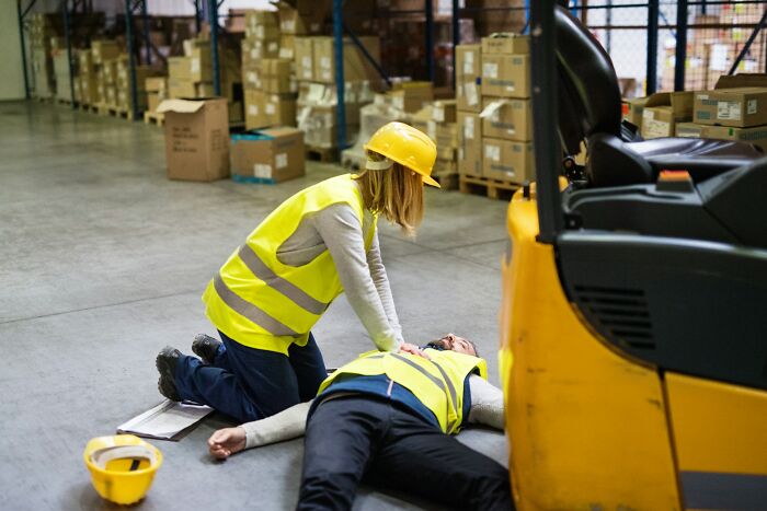 Worker administering first aid to unconscious coworker in warehouse, highlighting toxic workplace moments and safety risks.