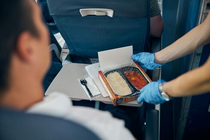 Flight attendant wearing gloves serving an in-flight meal to a passenger, highlighting underrated plane perks.