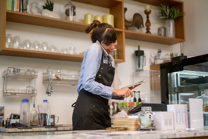 Woman multitasking in a cafe, holding a phone and tablet, highlighting dangerous things often dismissed at work.