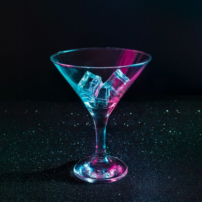 Martini glass with ice cubes illuminated by blue and pink neon lights against a dark background, strange things concept.