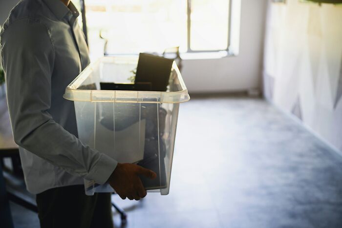 Man holding a clear plastic box with office items, symbolizing toxic workplace moments and employee challenges.