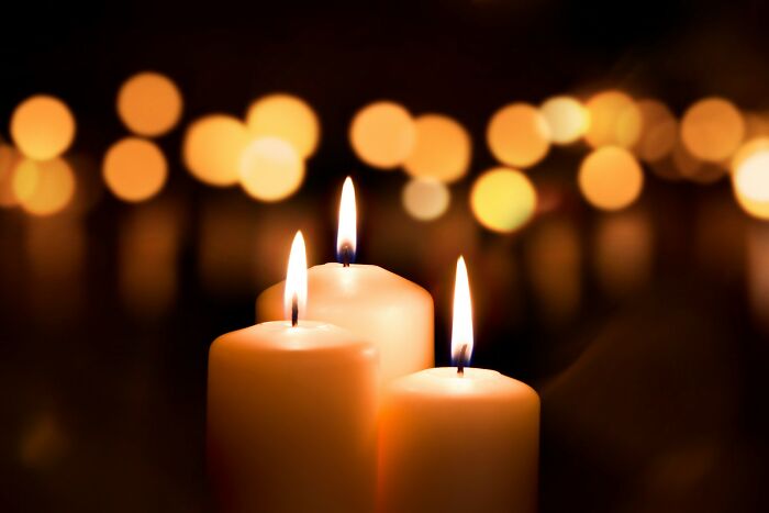 Three glowing candles with blurred warm lights in the background, evoking strange things people witnessed.