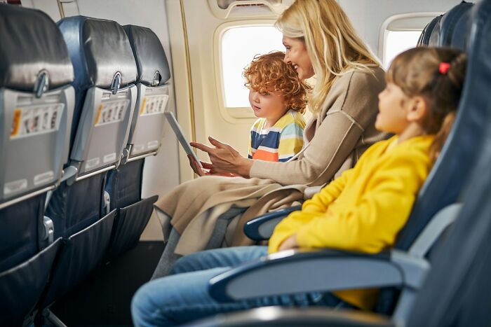 Mother and children sitting in airplane seats, using a tablet, illustrating underrated plane perks on a flight.