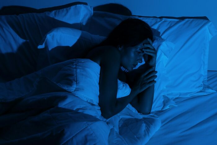 Woman lying awake in bed at night looking worried, reflecting on strange things people witnessed that made them question everything.