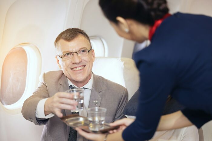 Man in business attire smiling and receiving a drink from flight attendant showcasing underrated plane perks on flight.