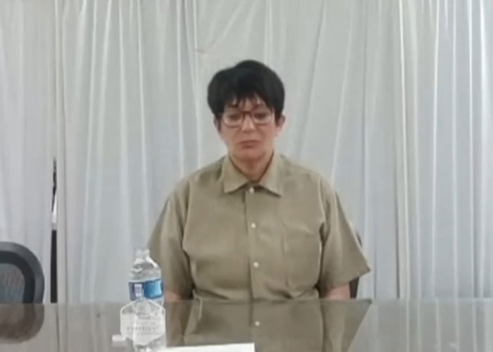 Former inmate wearing glasses and prison uniform sitting at a table, sharing foul details about Ghislaine Maxwell in prison. Former inmate wearing glasses and prison uniform sitting at a table, sharing foul details about Ghislaine Maxwell in prison.