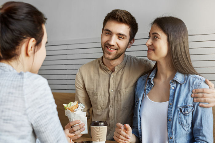 Couple sitting at a caf&eacute; smiling at a female server, highlighting girlfriend disrespect in the service industry setting.