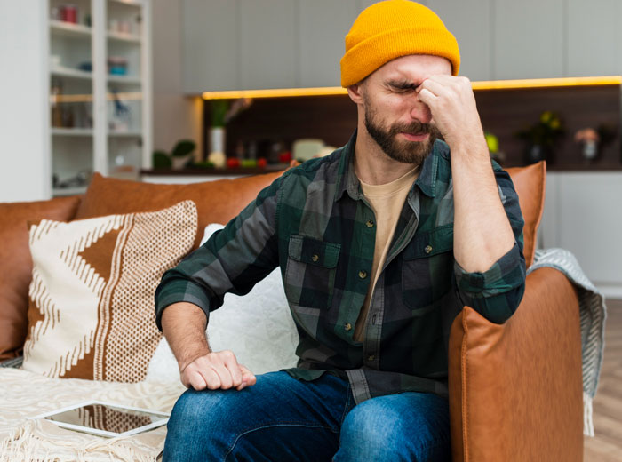 Man in a yellow beanie sitting on a couch looking frustrated, representing an electrician's emotional moment.