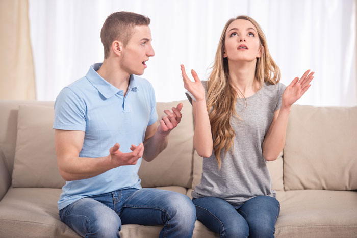 Couple arguing on a couch with the man upset and woman appearing frustrated, highlighting controlling girlfriend conflict.