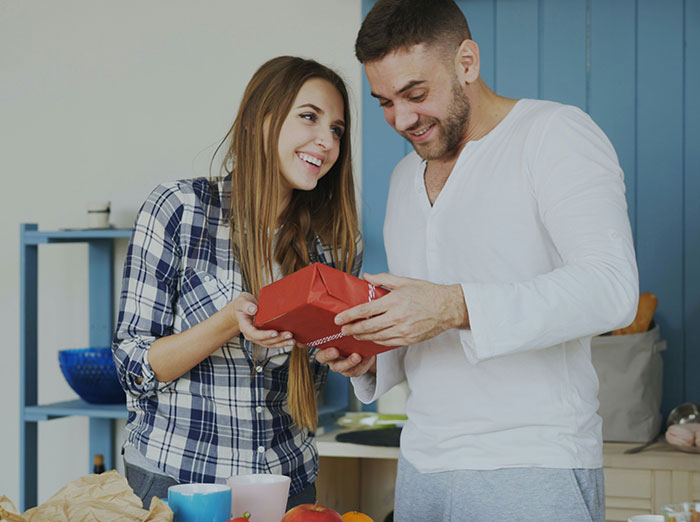 Woman upset as boyfriend happily accepts her gift, showing mixed emotions in a casual home setting.