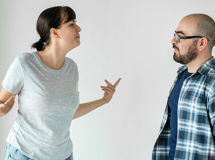 Woman upset as boyfriend likes her gift, standing face to face in tense conversation against plain background.