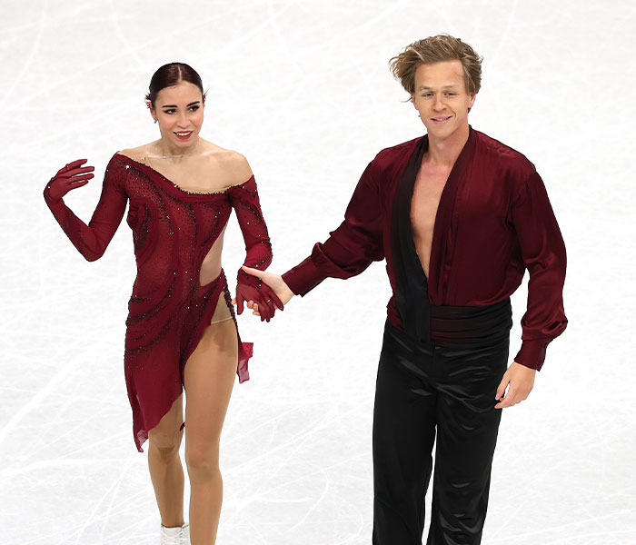 Figure skating duo in matching red costumes performing at the 2026 Winter Olympics during a wild and bizarre moment.