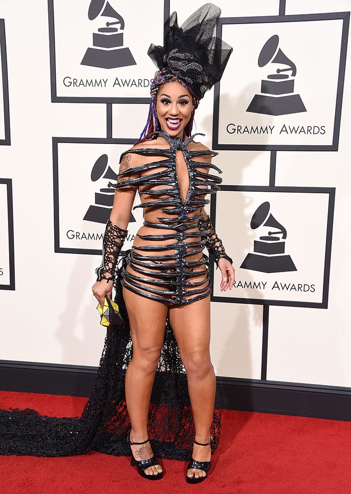 Woman in a striking black cutout dress and headpiece posing on the red carpet at the 2016 Grammys fashion event.