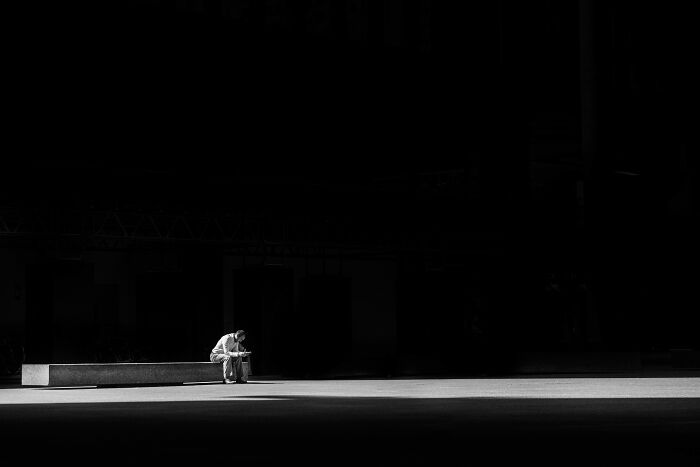 A person sitting alone on a bench in a large dark space, reflecting on time and energy challenges.