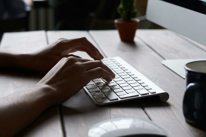 Hands typing on a keyboard at a wooden desk, symbolizing the struggle between time and energy management.