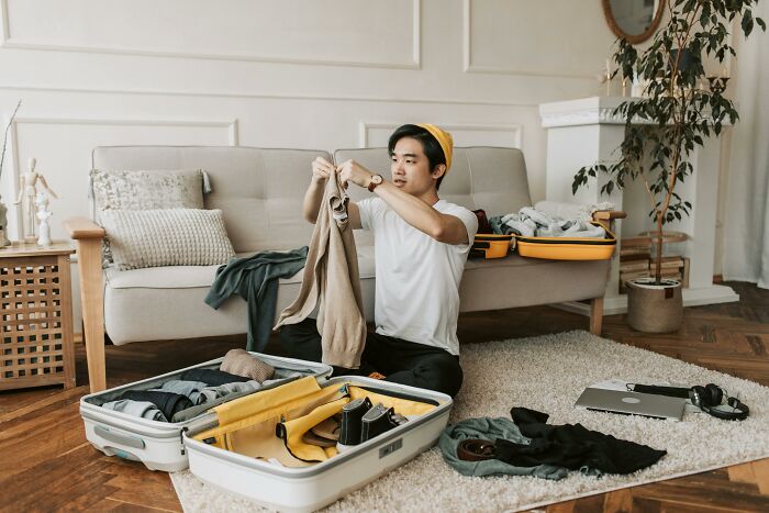 Young man packing clothes into a suitcase, facing the challenge of balancing time and energy in daily life.