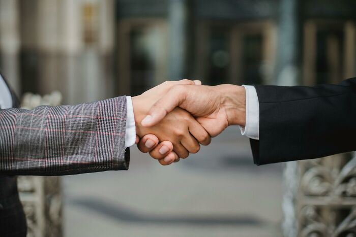 Two people shaking hands in a business setting representing time and energy balance negotiations.