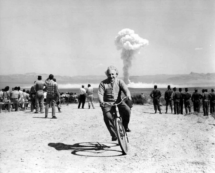 Albert Einstein riding a bicycle near a distant nuclear explosion, a surreal scene that defies explanation without Photoshop.