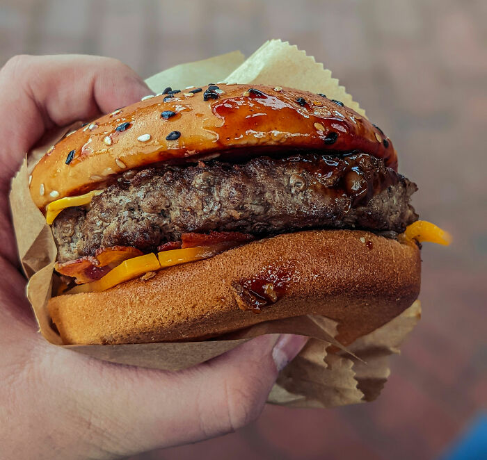 Hand holding a close-up of a hamburger, unrelated to colon cancer breakthrough keywords in the image context.