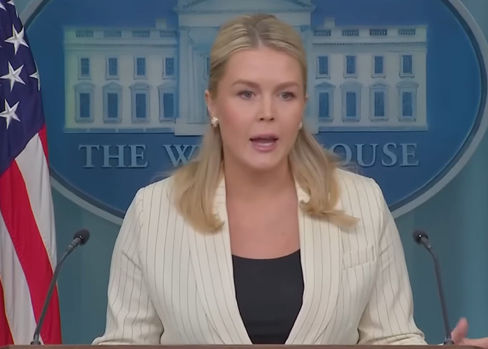Woman in a white blazer speaking at a podium with US flag and White House backdrop about bitcoin exchange and police control.