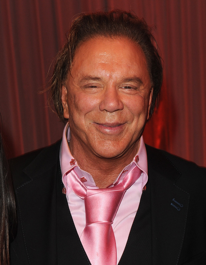 Mickey Rourke smiling at an event, wearing a pink shirt and tie, with natural aging and no cosmetic procedures.